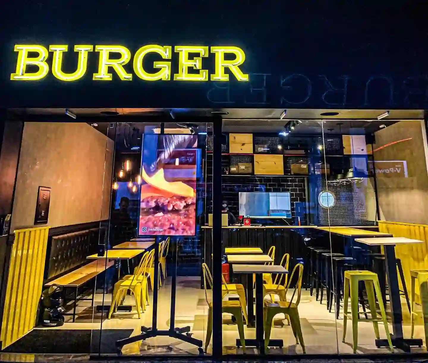 Fachada do The Vila Burger à noite, com letreiro luminoso BURGER